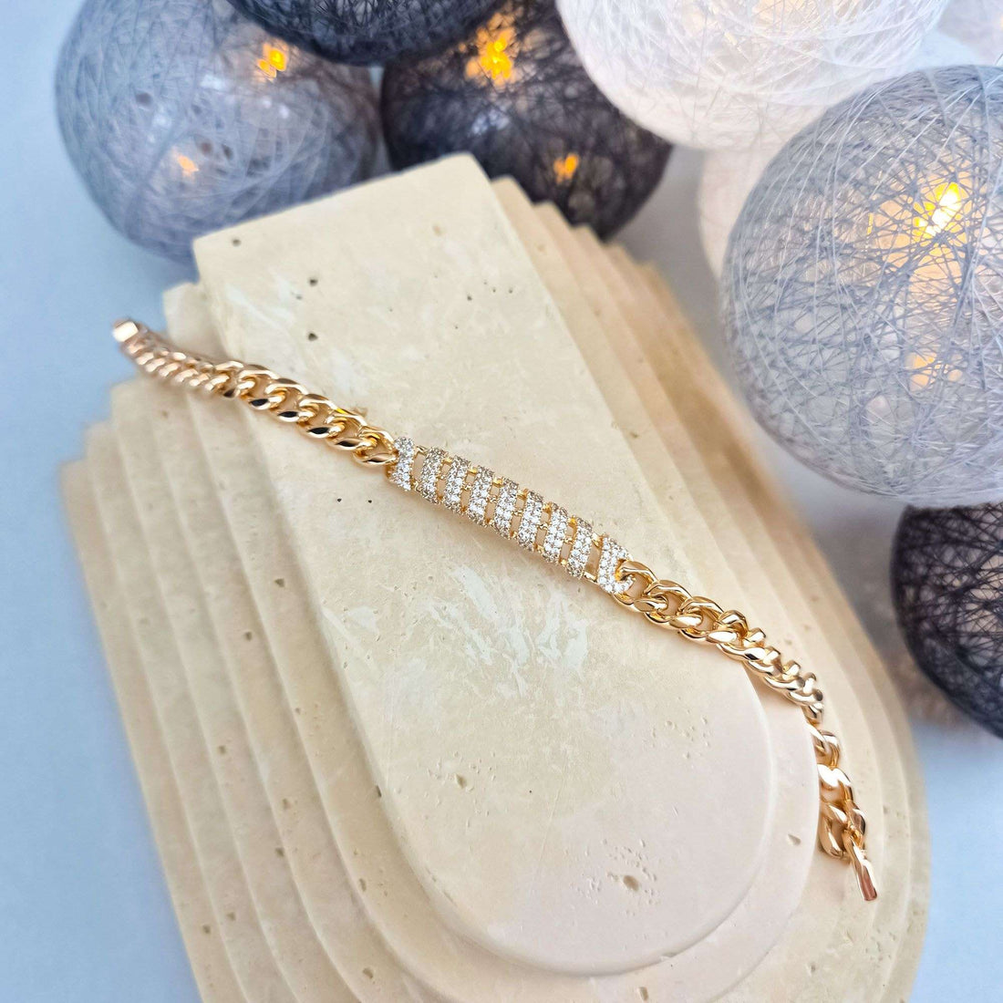 Chunky gold-tone chain bracelet with cubic zirconia centre link on a stone stand
