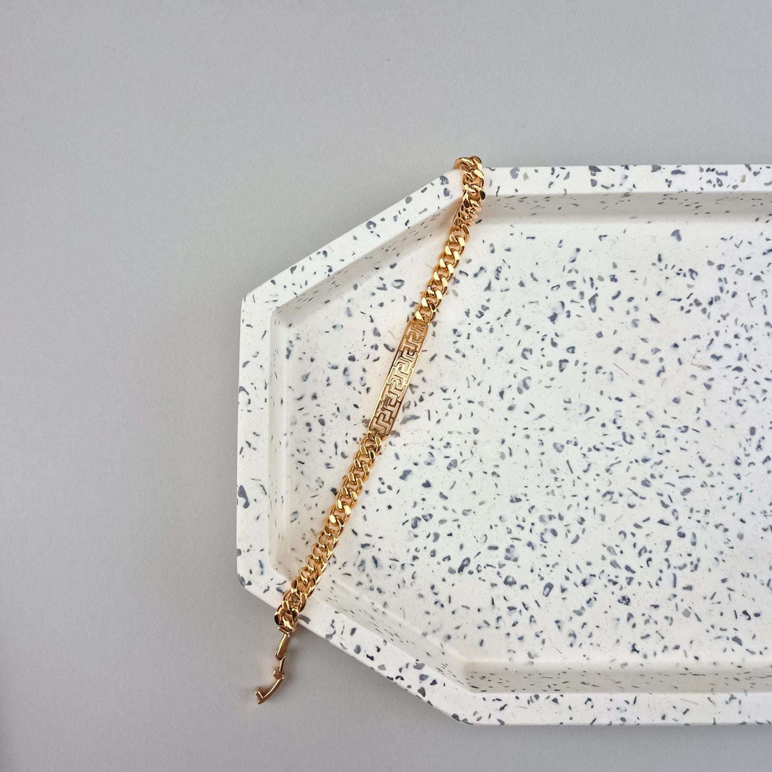 Gold-tone chain bracelet with meander-cut plate on a speckled tray