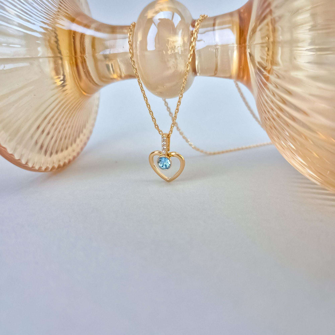 Gold-tone chain with a heart pendant and blue crystal beside a glass vase