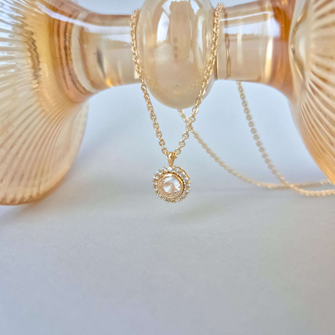 Close-up of a gold-plated halo pendant necklace over an amber glass vase