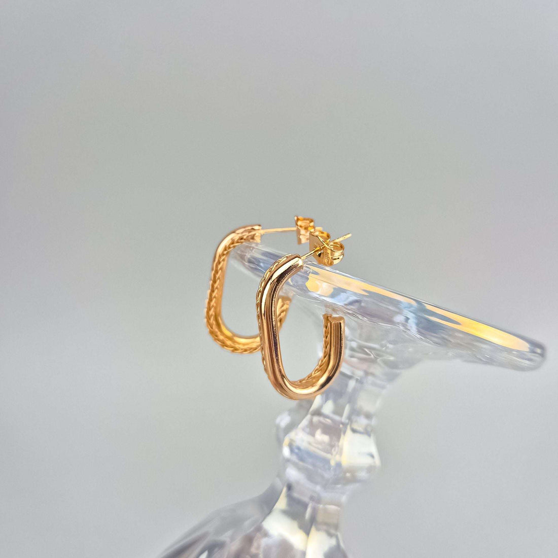Gold-plated woven hoops in side view on a crystal dish, push-back visible