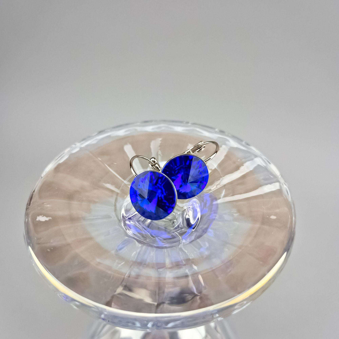 Blue crystal earrings on a clear glass stand, close side view