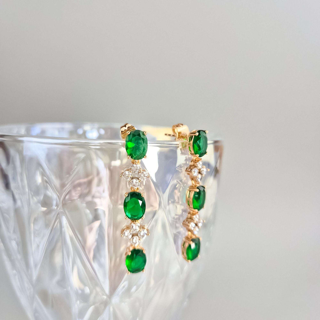 Green oval earrings resting against the rim of a cut-glass bowl