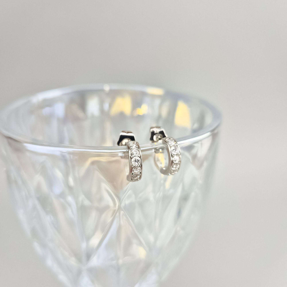 Cubic zirconia hoop earrings resting against the rim of a crystal glass