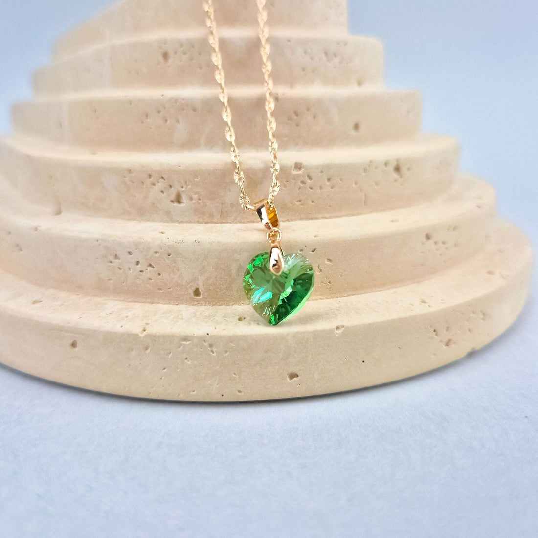 Close-up of the green heart crystal on a sand-coloured stand, gold-plated bail visible