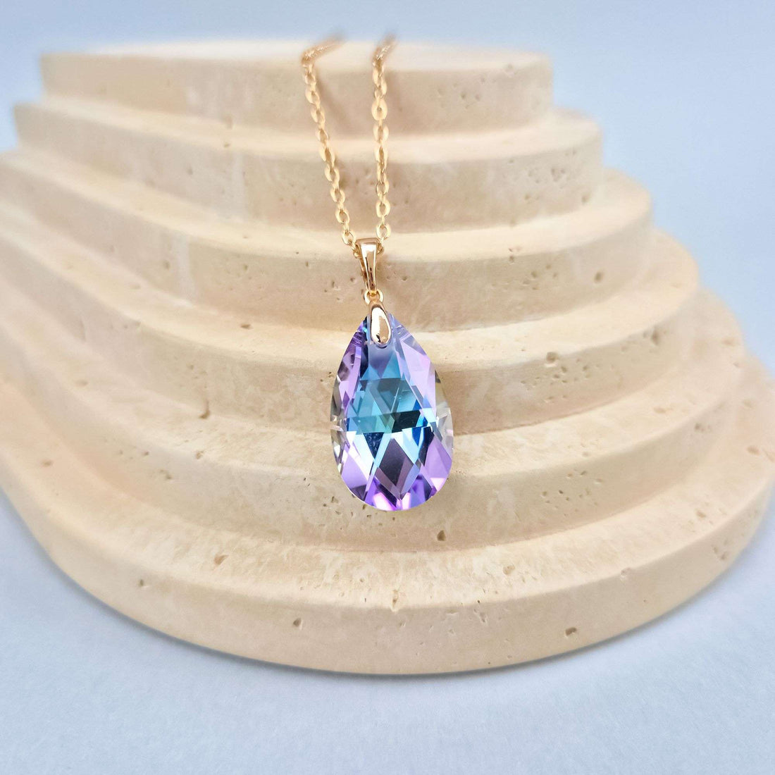 Teardrop crystal in blue and violet tones on a stone stand, side view
