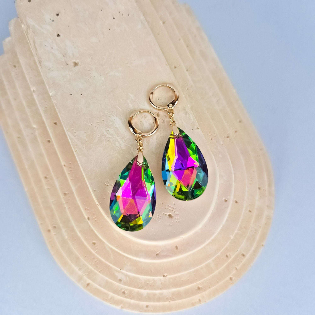 Multicoloured teardrop earrings on a beige stone stand, gold-plated French hooks visible