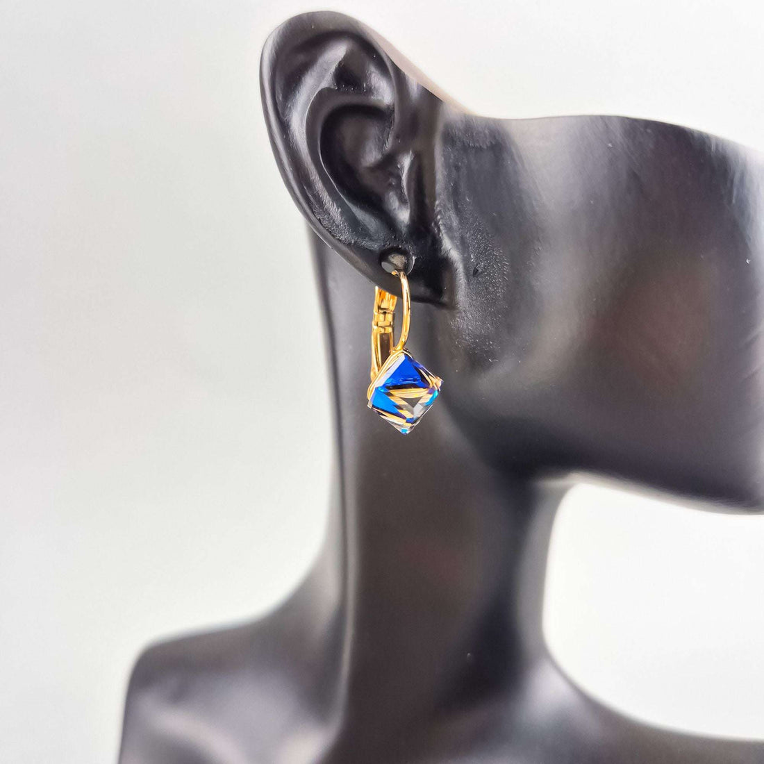 Blue-violet cube crystal earring with a gold-plated hook on a black mannequin ear
