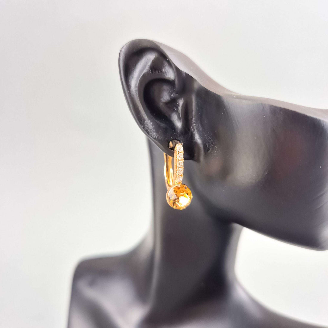 Yellow crystal earring with cubic zirconia on a black mannequin ear, side view