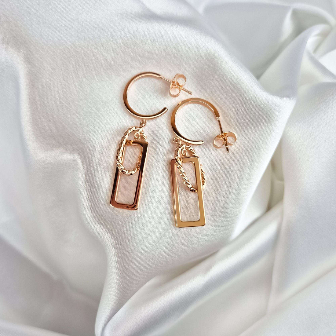 Geometric rose gold-tone earrings on white satin showing push-back fastenings