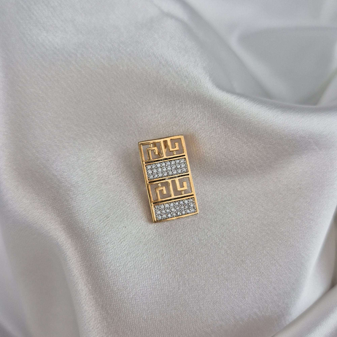 Geometric meander pendant in gold tone shown at an angle on white silk