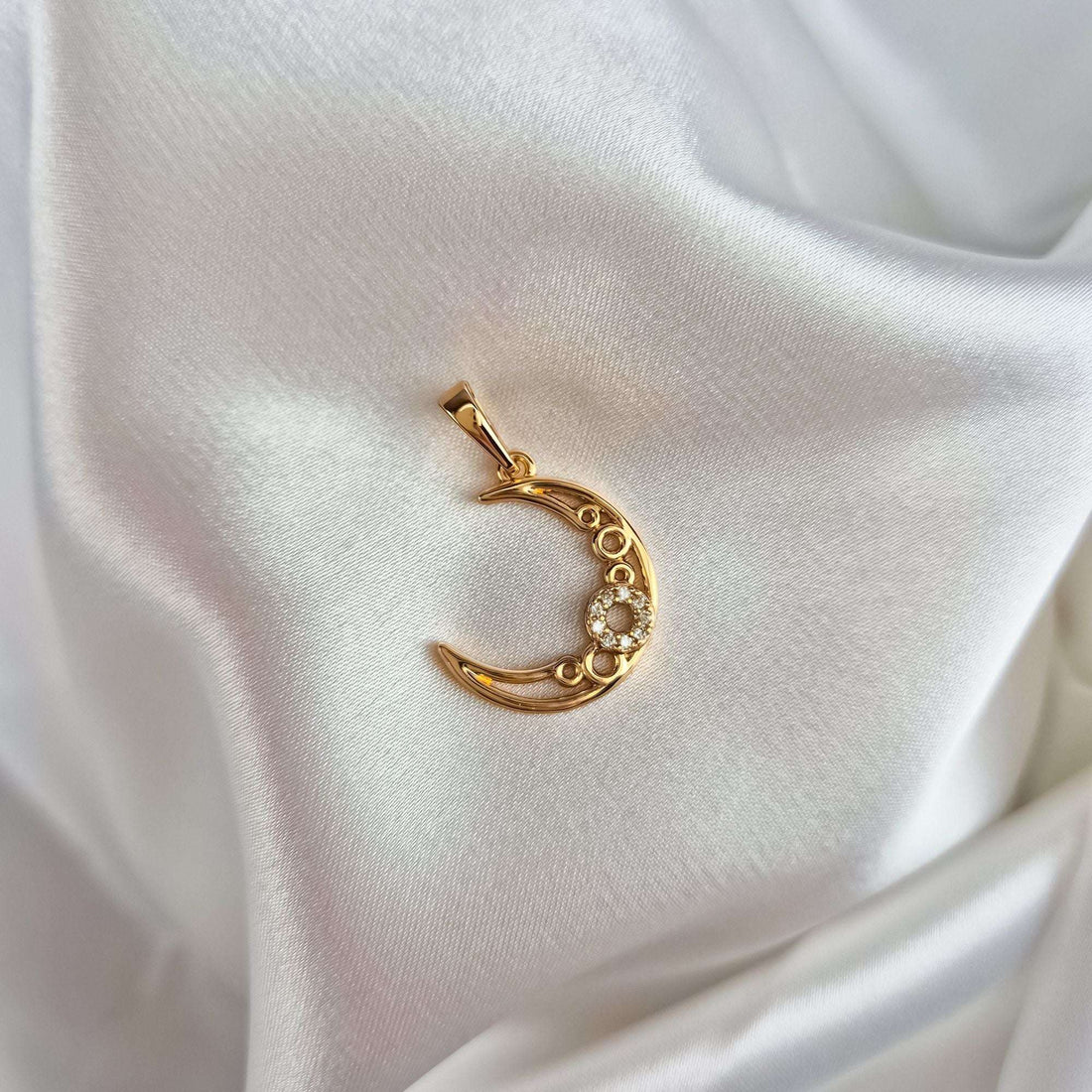 Gold-tone crescent pendant with cubic zirconia lying on white silk