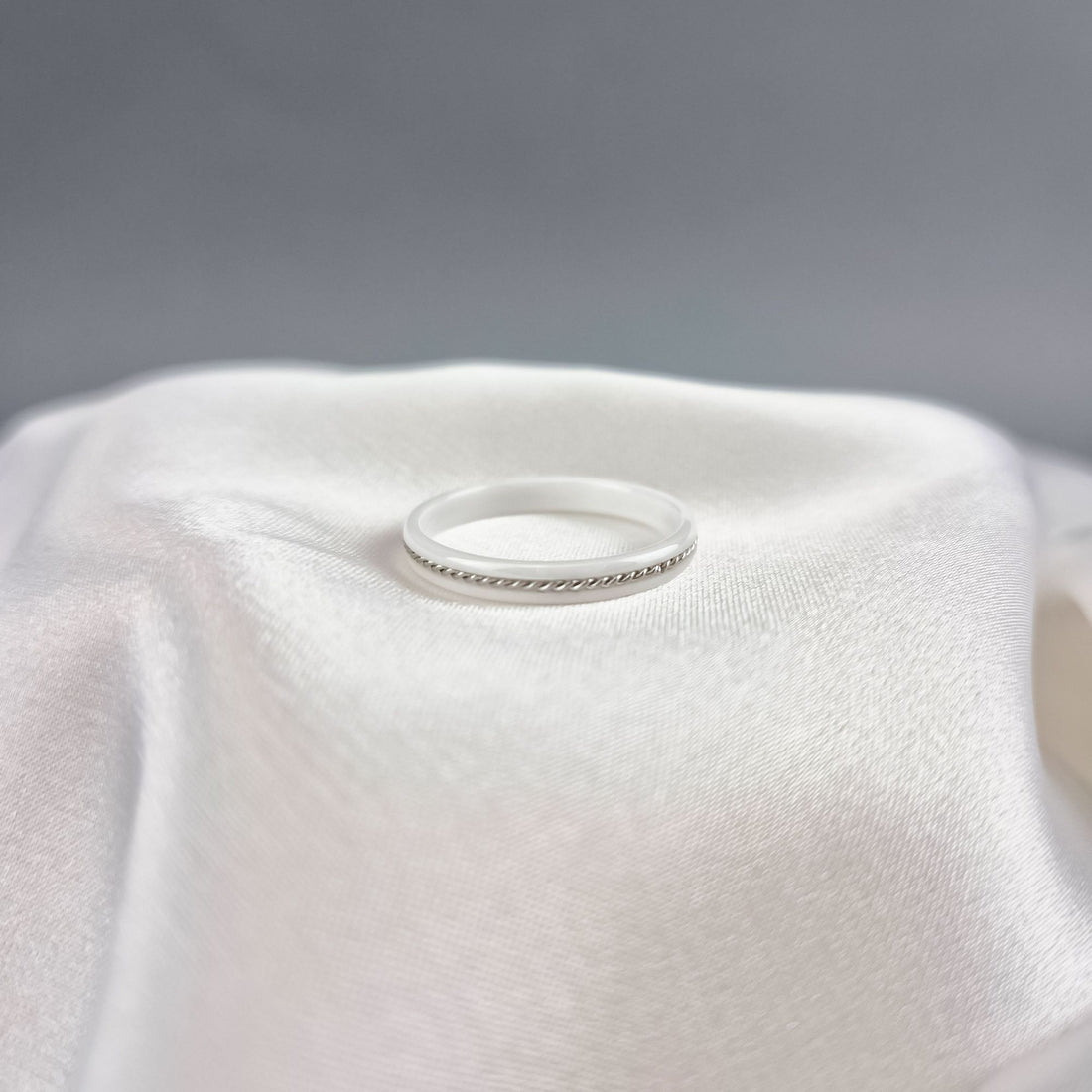 White ceramic ring with twisted metal detail resting on soft white fabric