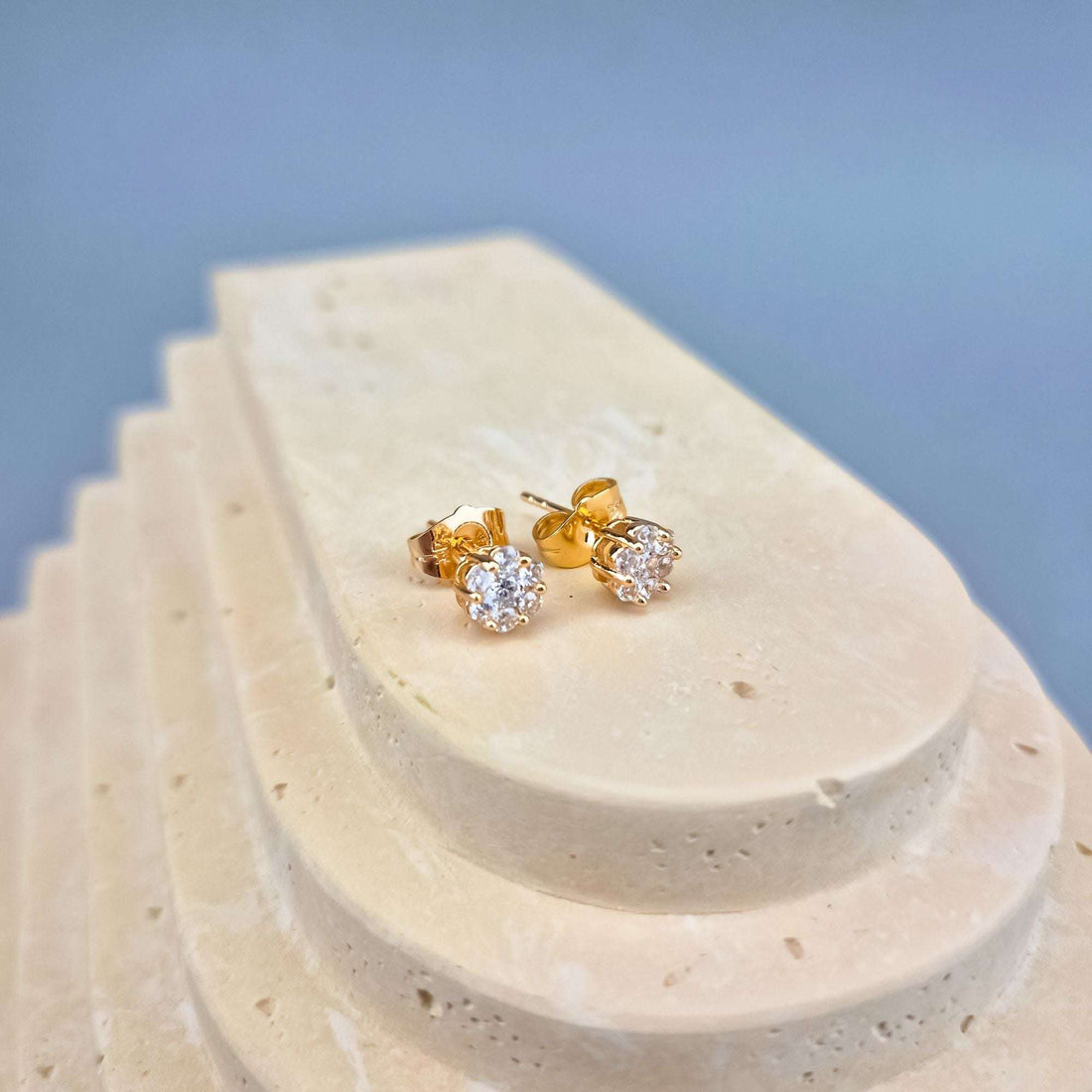 Side view of gold-tone flower studs on a stone slab, push-back fastening visible