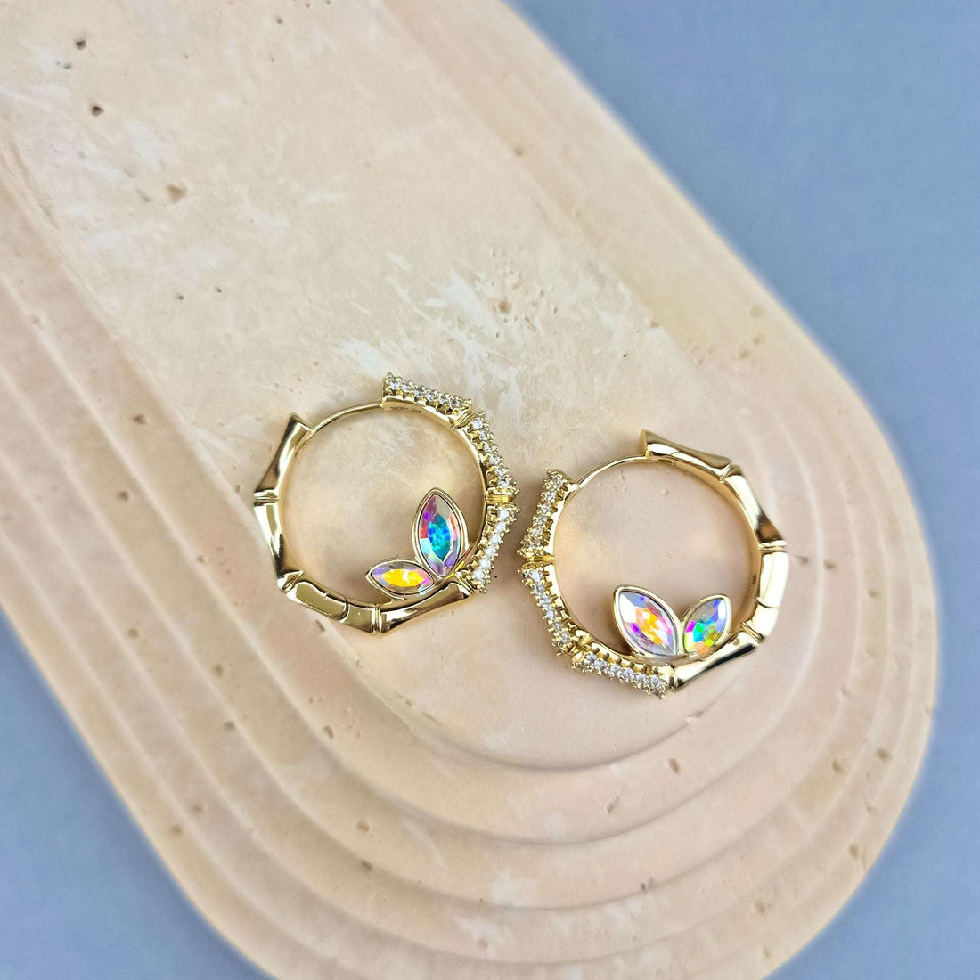 Pair of gold-tone hoop earrings with multicoloured crystals on a beige stand