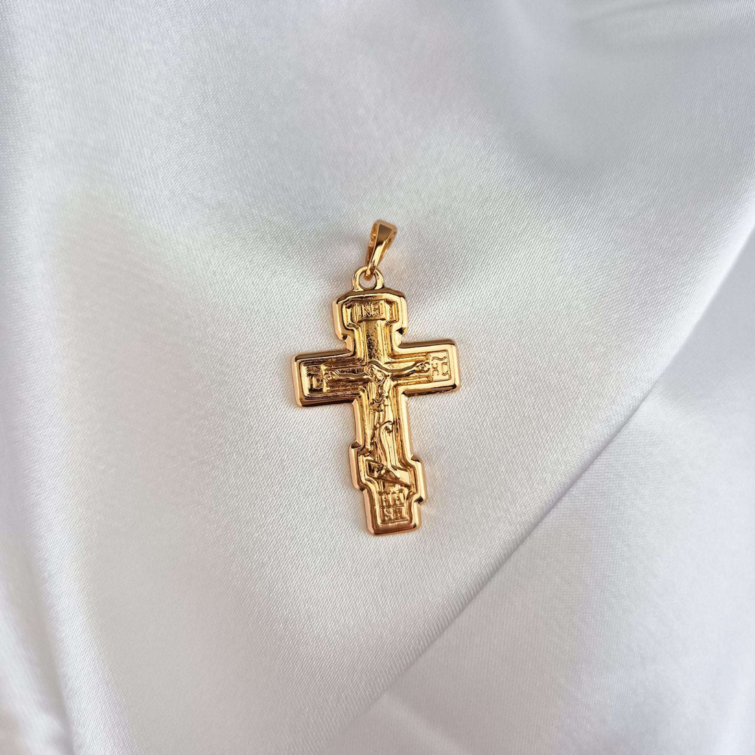 Gold-plated Orthodox cross with a loop, photographed at an angle on white satin