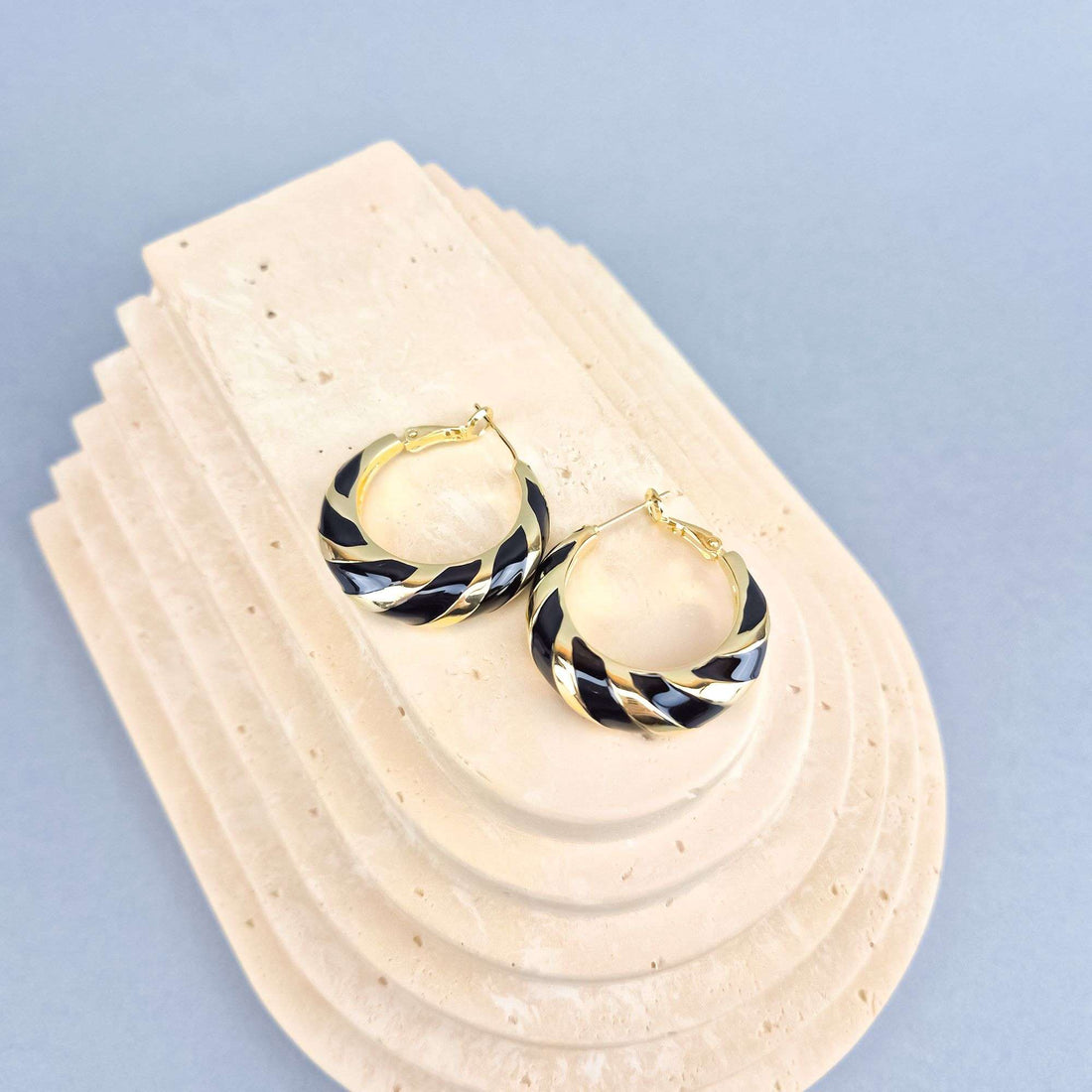 Black and gold-tone striped round earrings on a sand-coloured stone stand