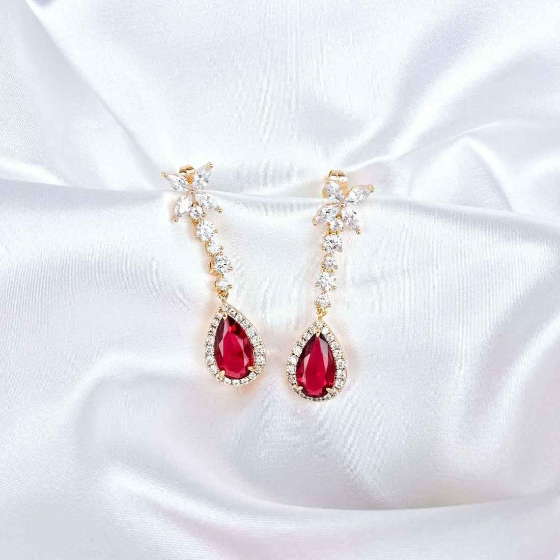 Evening earrings with a red teardrop stone and gold plating on white satin