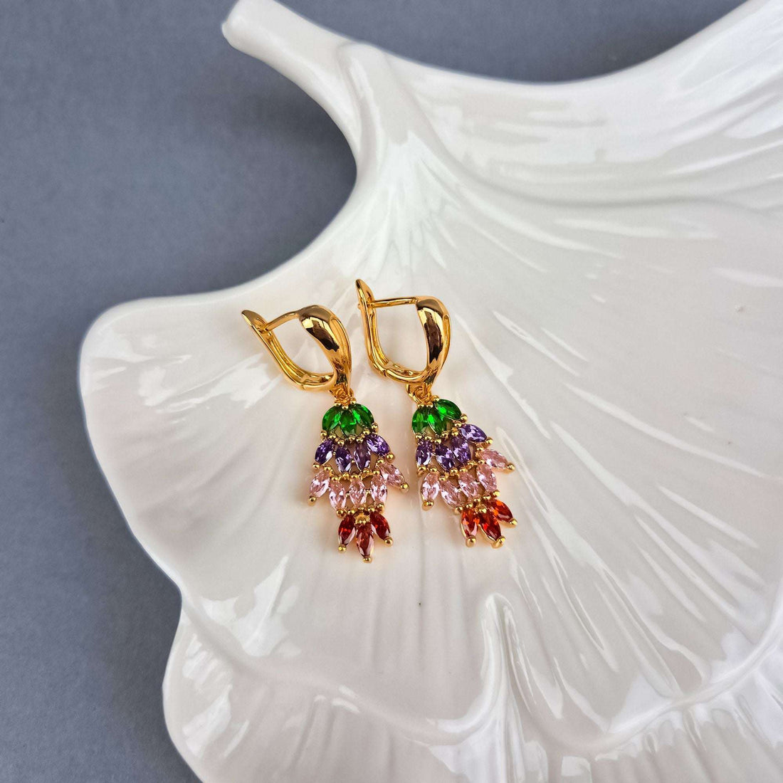 Colourful gold-plated drop earrings on a ceramic plate