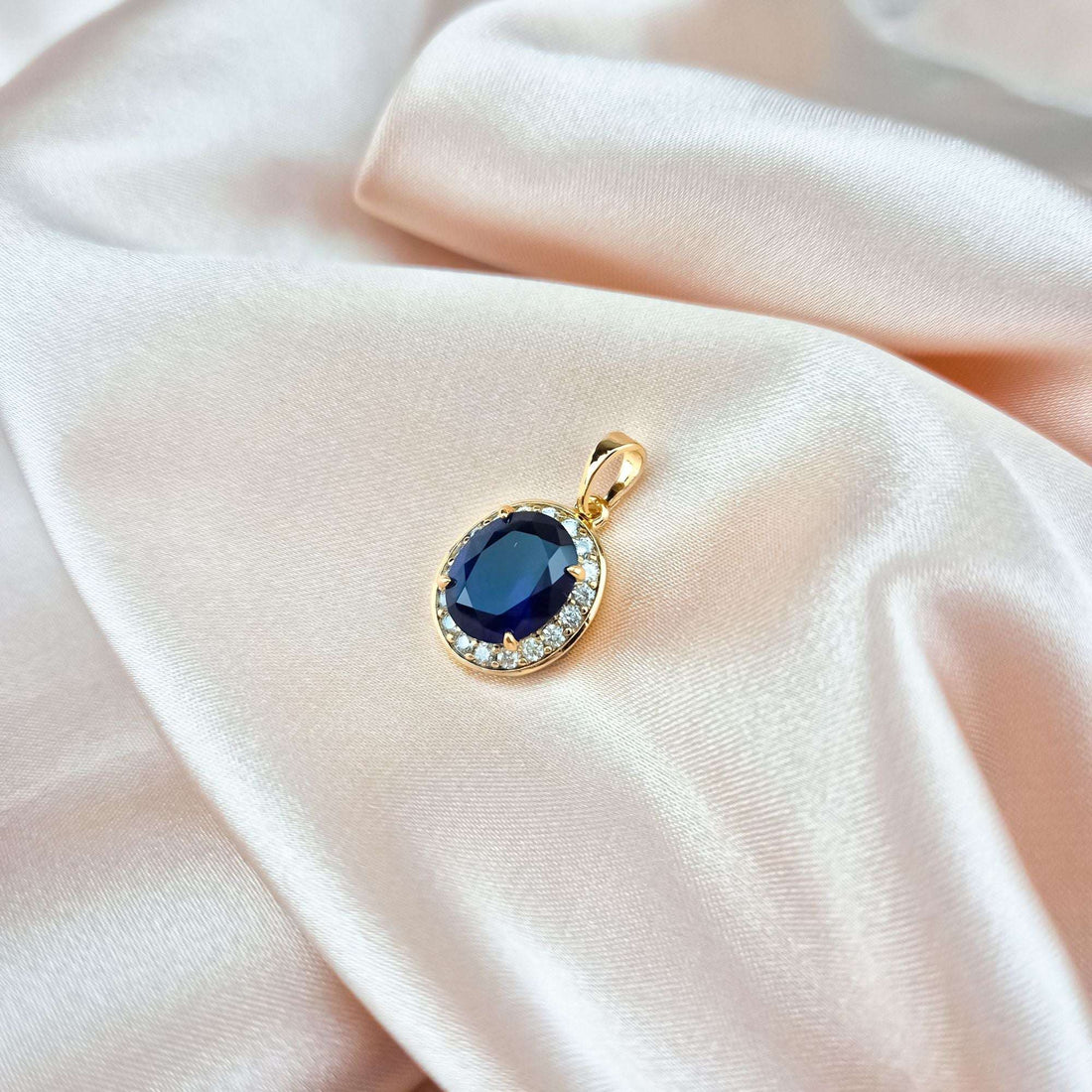 Dark blue stone pendant in gold-tone setting, close-up on cream silk