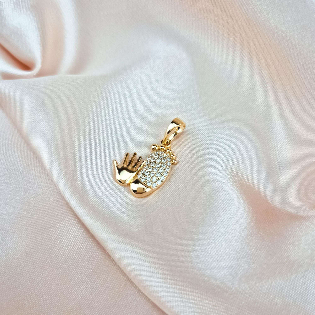 Close-up of the small feet and hand pendant on pale pink silk