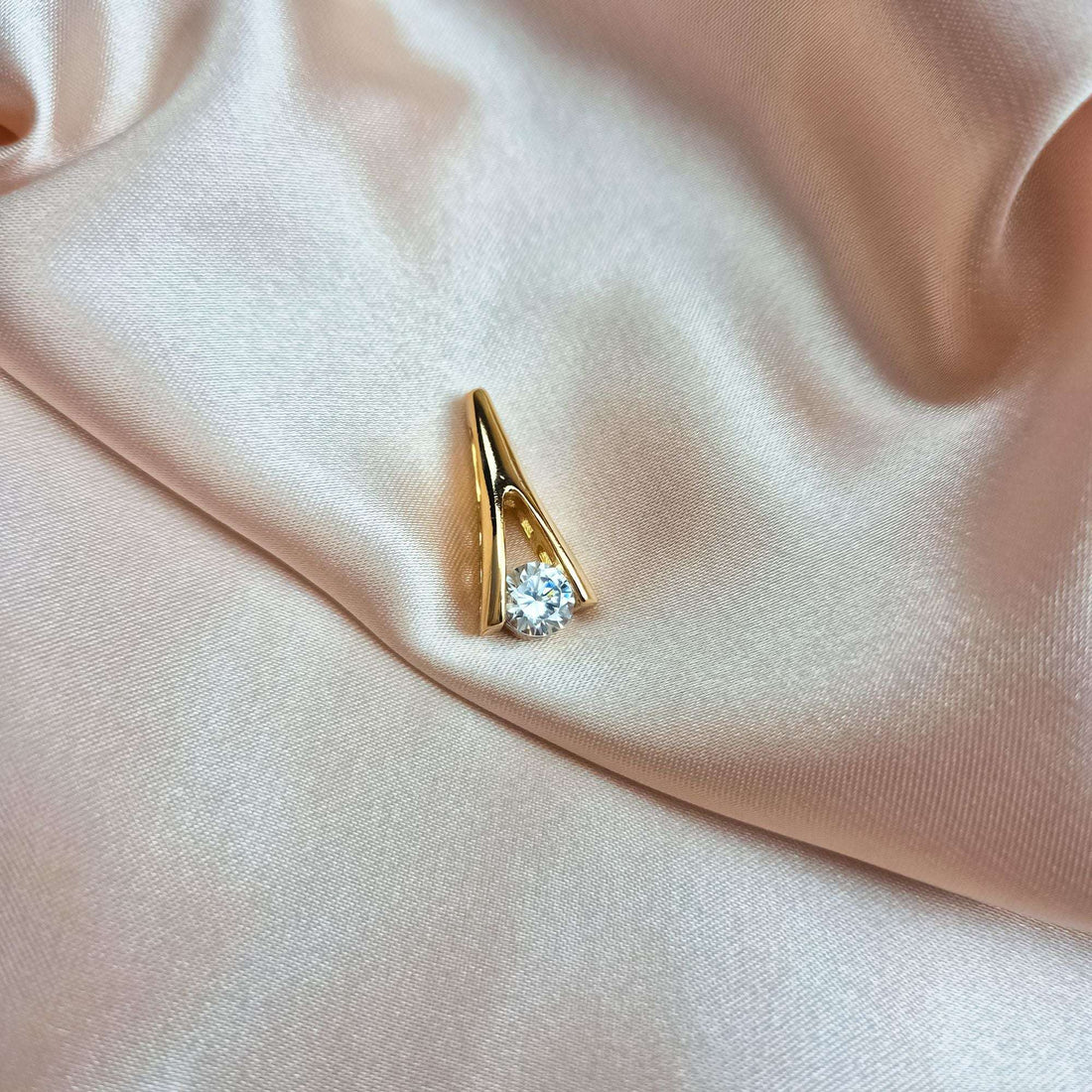 Gold-tone pendant with a clear stone lying on cream silk