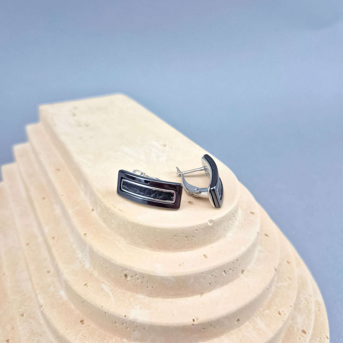 Black ceramic earrings on a sand-coloured stone stand, steel leverback clasp visible