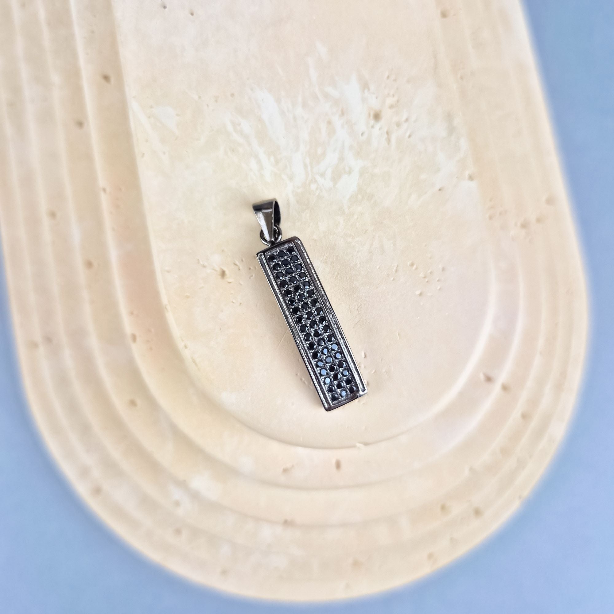 Taisnstūra formas sudraba kulons (32 mm) ar melno akmentiņu rindu.