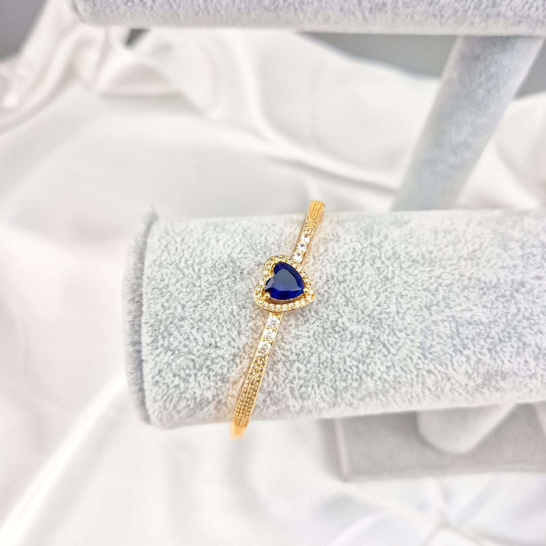 Rigid gold-plated bangle with a blue heart and sparkling stone band, on display