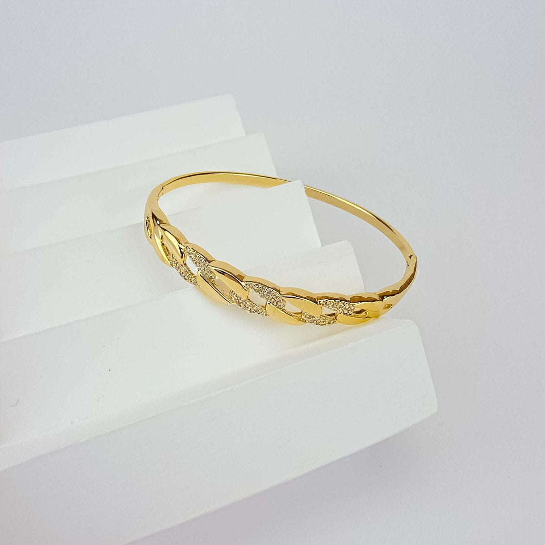 Gold-tone chain-link bangle with sparkling cubic zirconia on a white stand