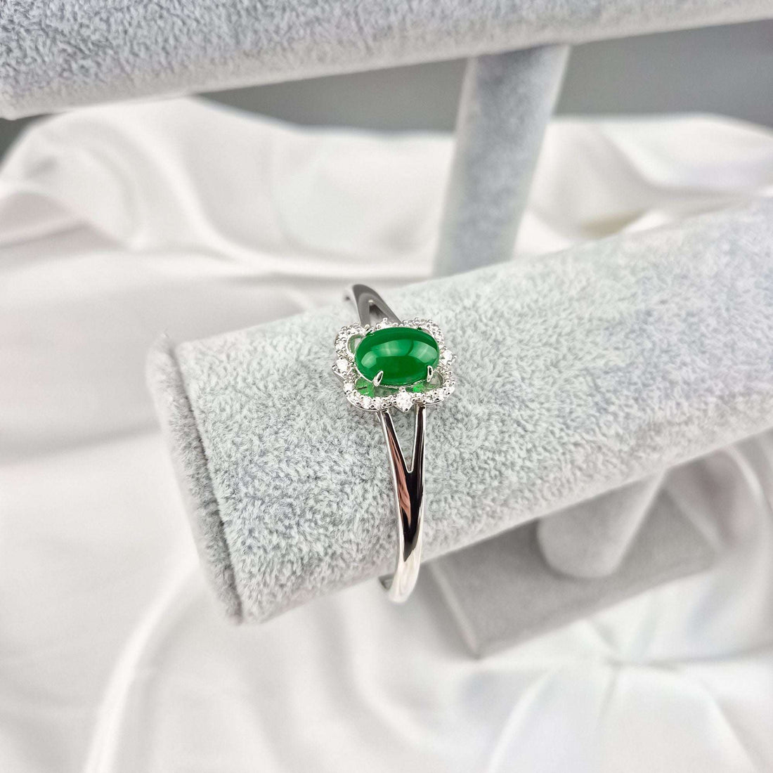 Green stone bangle in silver tone, close-up on a light grey velvet stand