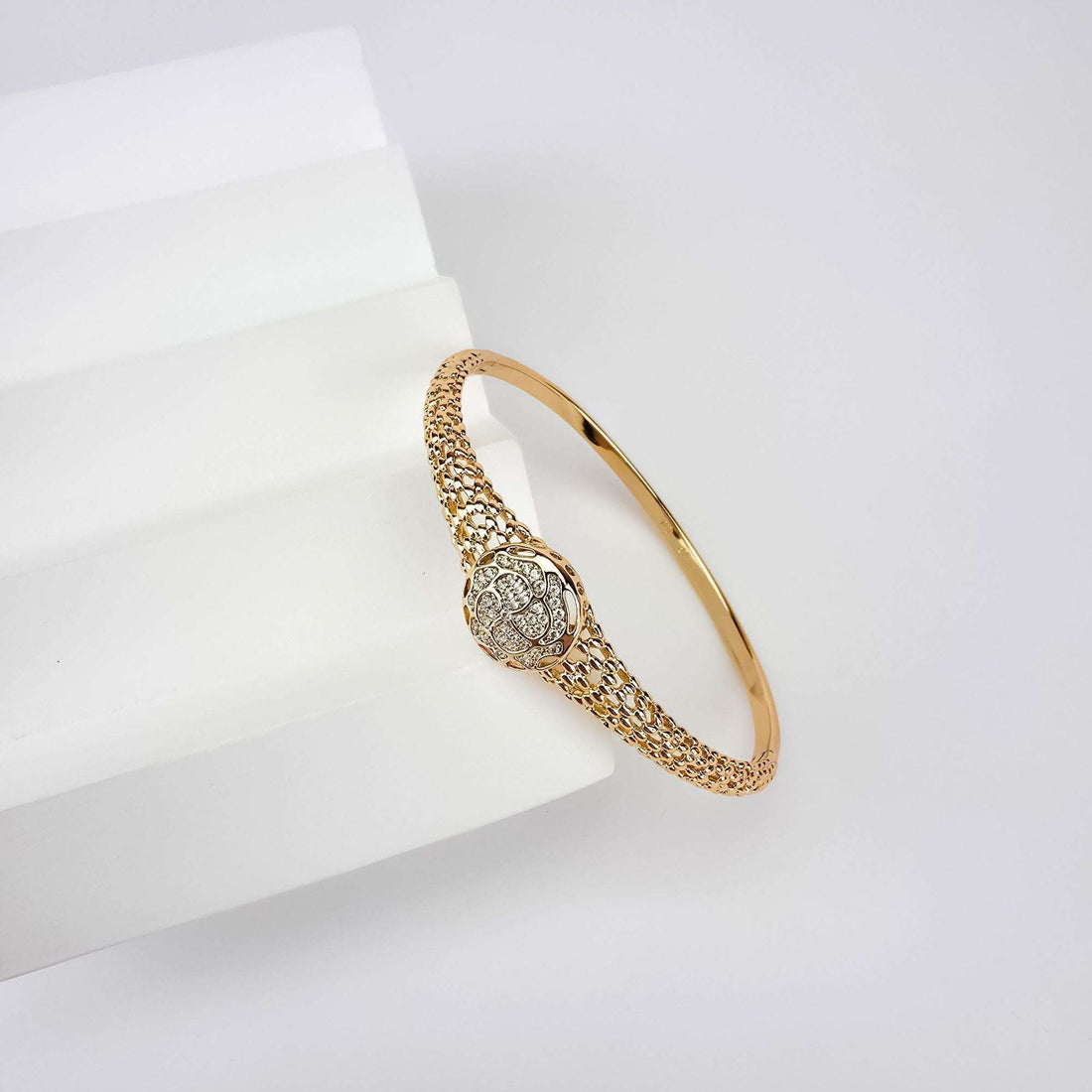 Gold-tone mesh bangle on a white block with a sparkling rose medallion