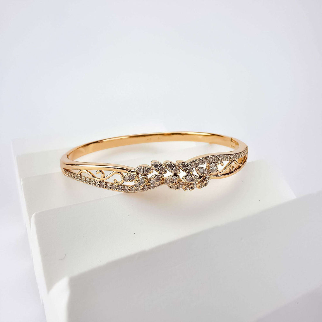 Gold-plated filigree bangle with cubic zirconia, angled on a white block