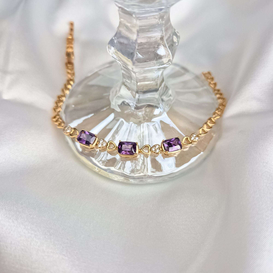 Close-up of a gold-plated bracelet with violet crystals on a glass candleholder