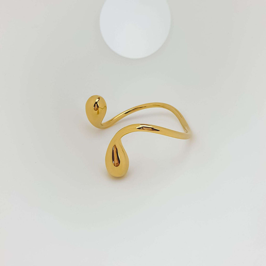 Gold-plated open bangle at an angle with shiny drops and a wavy band