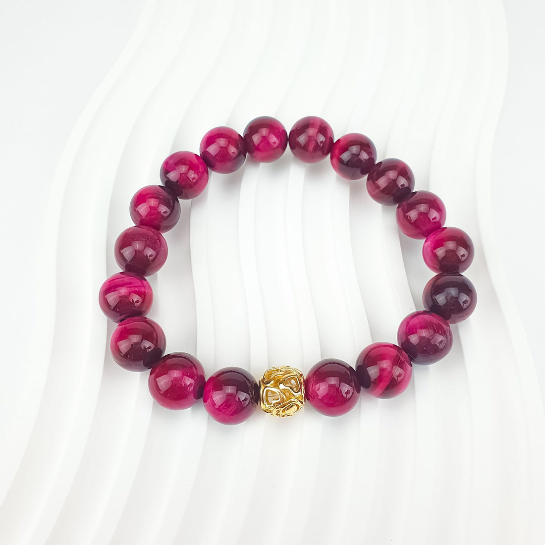 Pink tiger's eye bracelet on a white wavy background with gold-plated heart-pattern bead