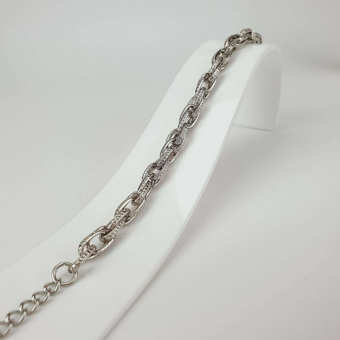 Close-up of the bracelet on a white stand, fine grained link pattern and extender
