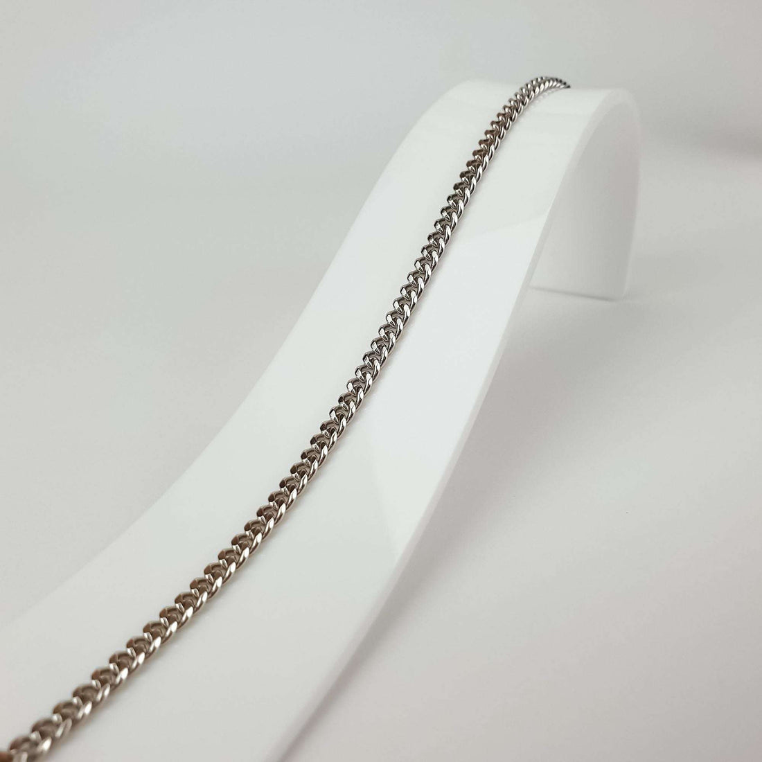 Close-up of the fine curb bracelet on a white stand, shiny silver-tone links