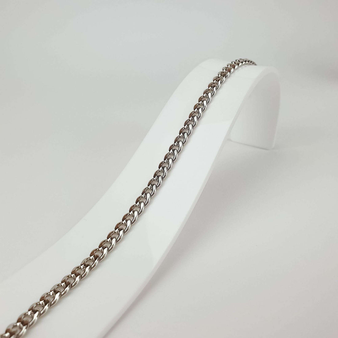 Wide curb bracelet on a white stand, side view of shiny links