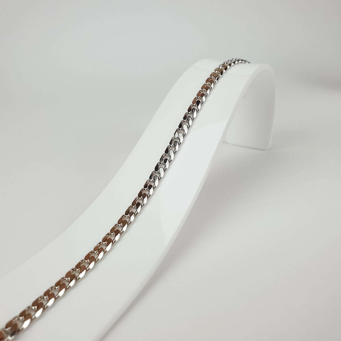 Silver-tone chain bracelet on a white stand, close-up of flat links