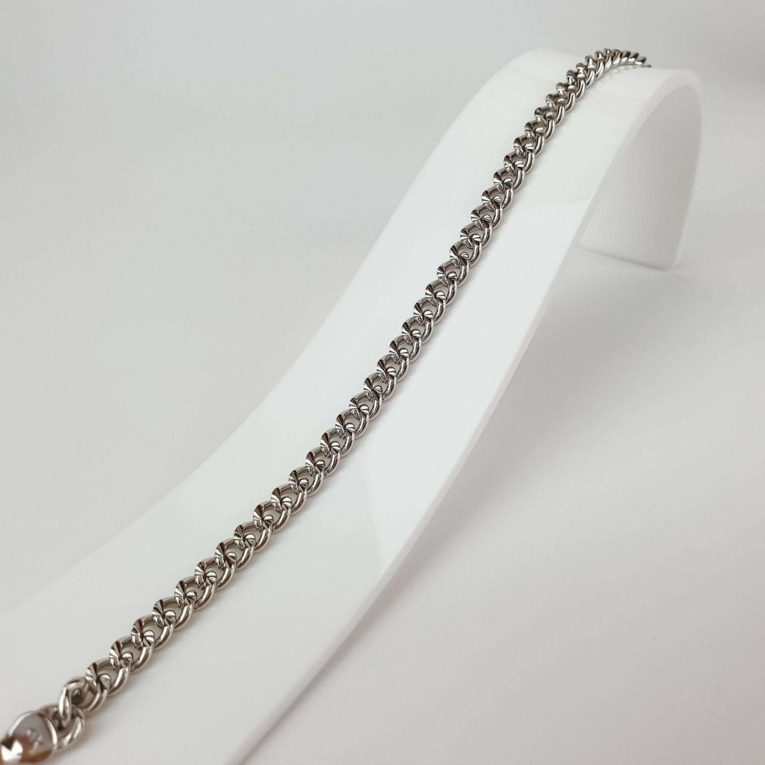 Close-up of the chain bracelet on a white stand, faceted links and lobster clasp