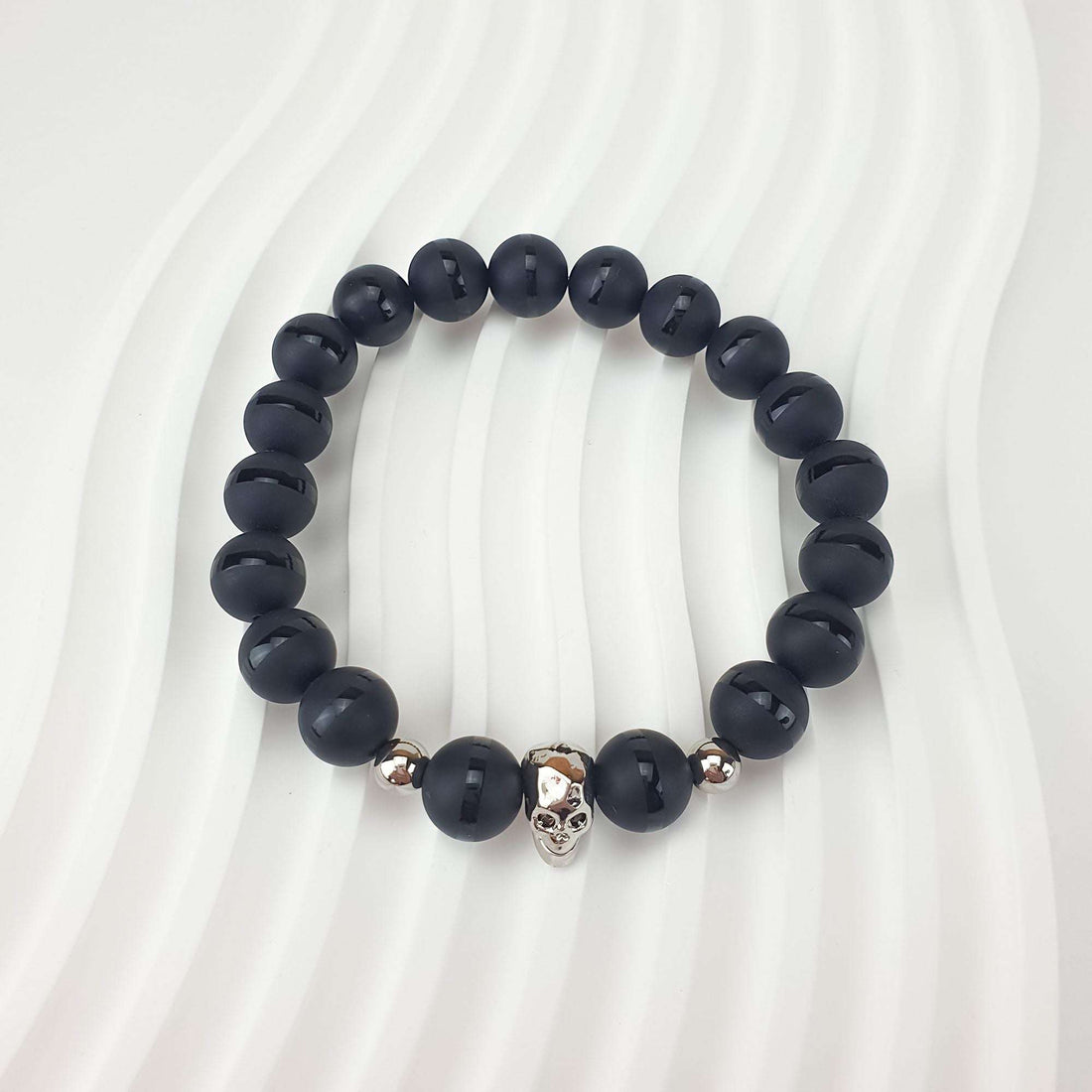 Close-up of matte black beads and a skull on a wavy white background