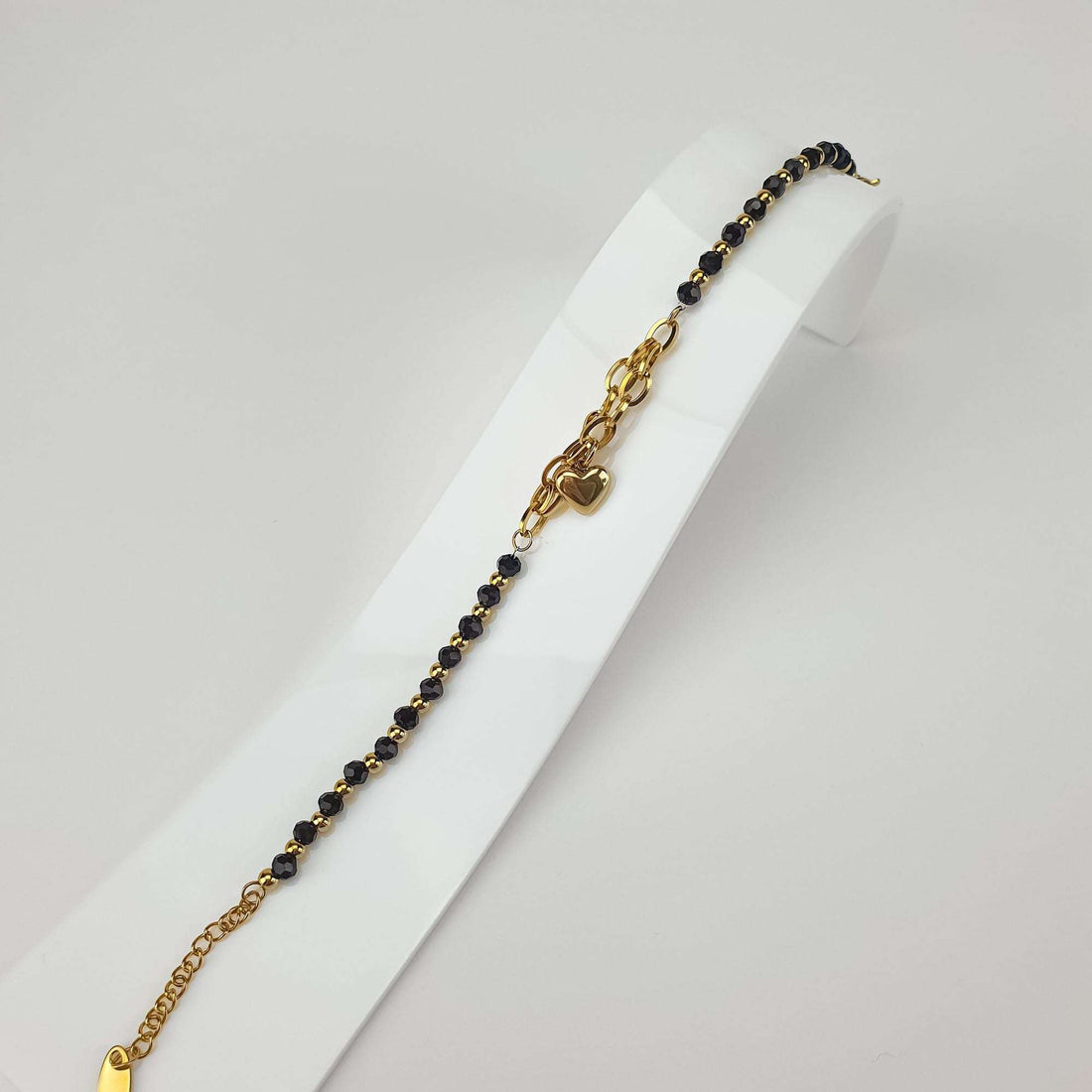Black bead and gold-plated bracelet on a white stand with adjustable extension chain