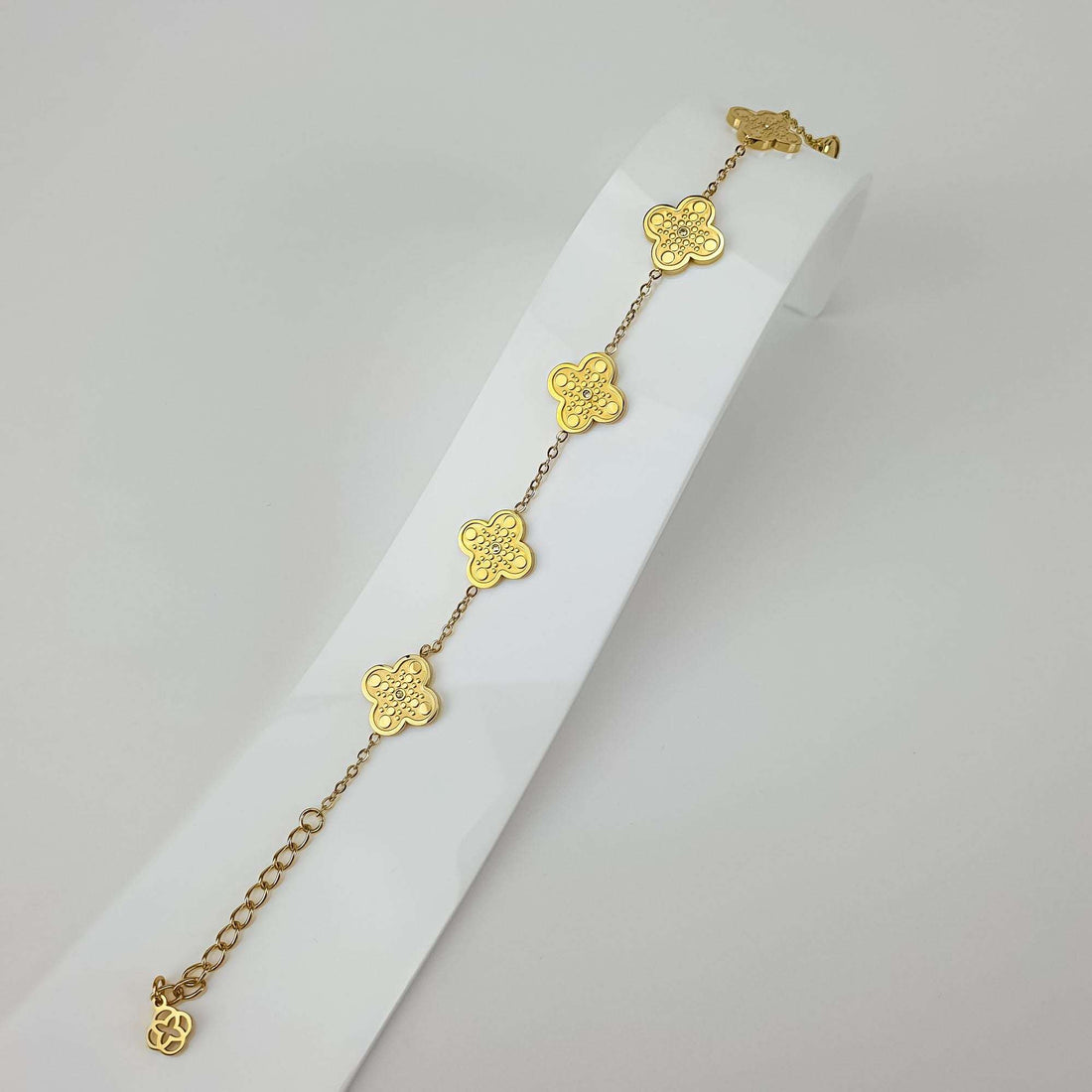 Gold-tone clover bracelet at an angle on a white stand with extension chain