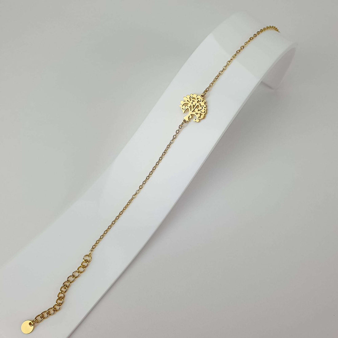 Delicate gold-plated tree of life bracelet stretched out on a white jewellery stand