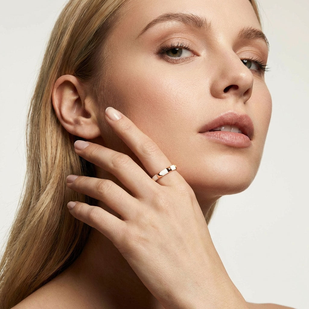 Model wearing a gold-plated white enamel ring, hand raised to her face