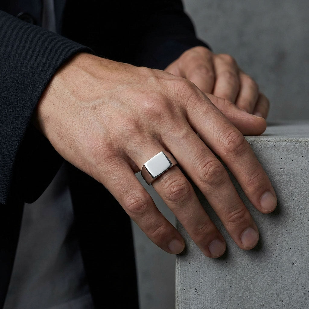 Man in a dark suit wearing a chunky steel signet ring, concrete backdrop