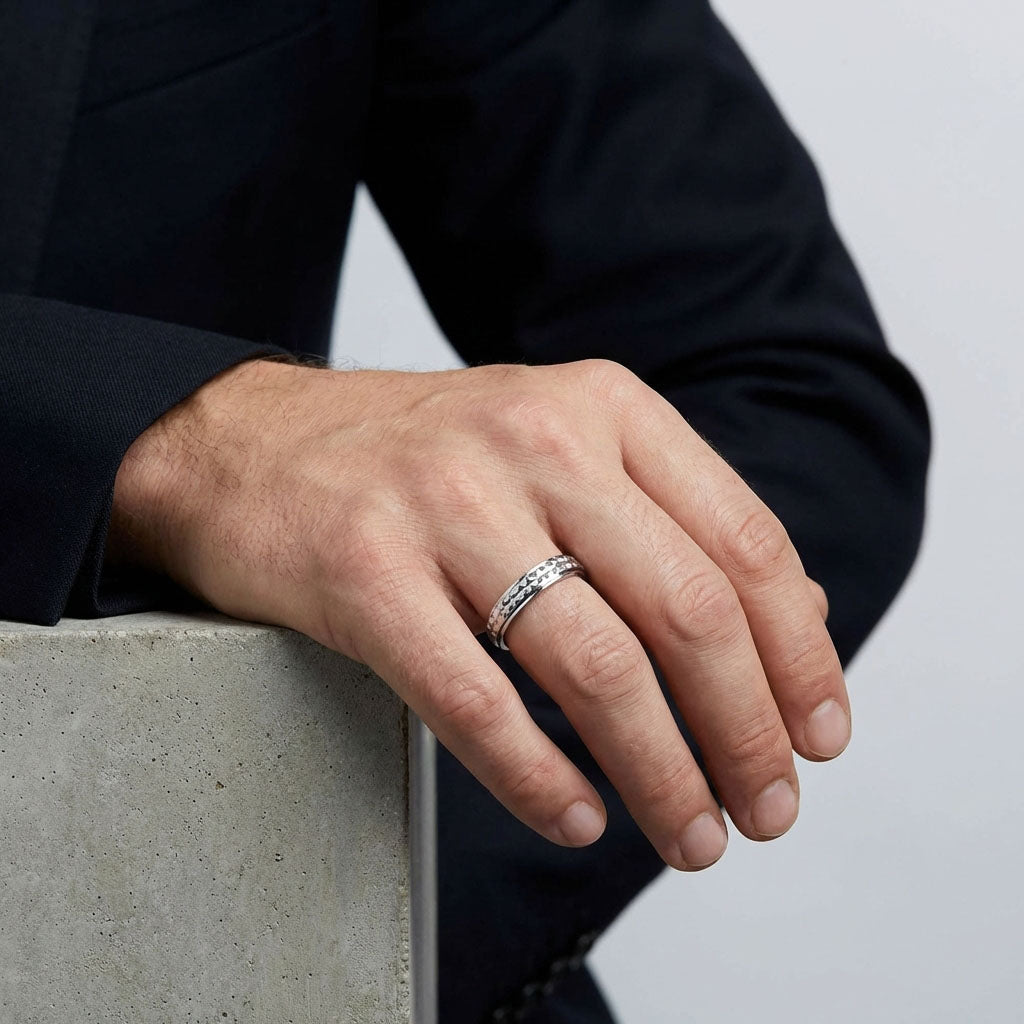 Man in a dark suit wearing the textured steel ring, hand on concrete