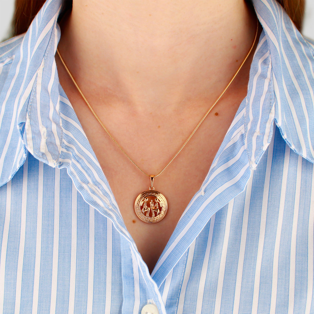 Fine gold-plated chain with a round zodiac pendant worn with a blue striped shirt