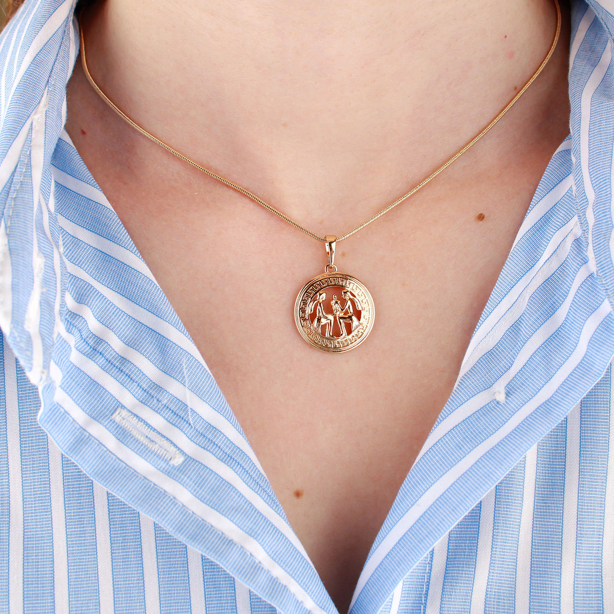 Fine gold-plated snake chain with a round pendant over a striped shirt